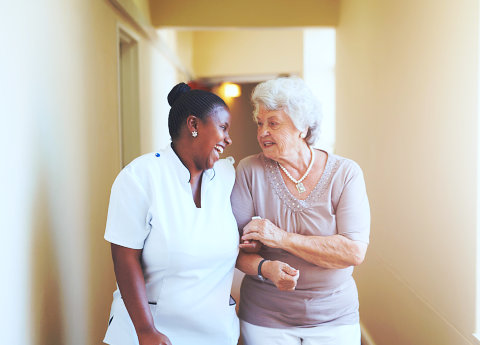 caregiver with elder woman walking side by side on a hallway