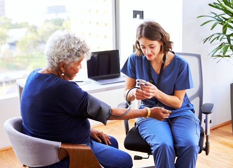 caregiver checking elder woman's blood pressure